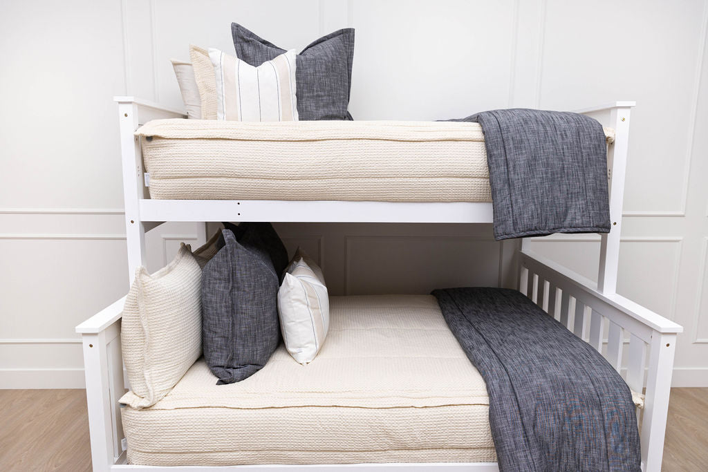 A standard bunk bed with both bunks made with cream waffle textured zipper bedding and charcoal dark gray and striped pillows and blankets.