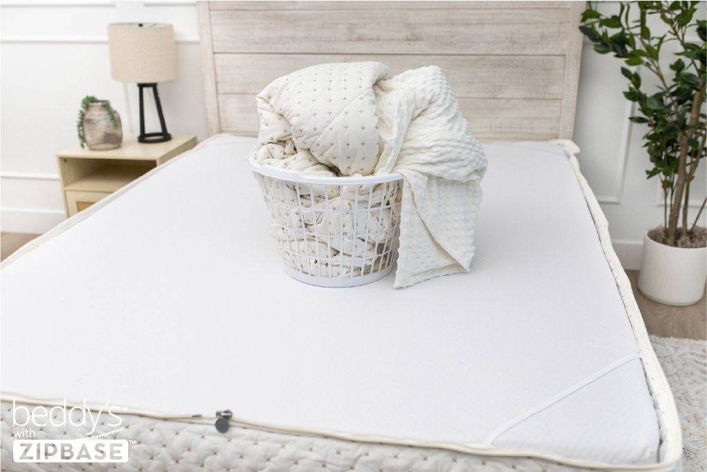 A bed made with just the fitted bedding base around the sides of the mattress, with the top comforter and ZipBase sheet in a basket on top of the bed.