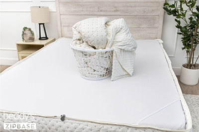A bed made with just the fitted bedding base around the sides of the mattress, with the top comforter and ZipBase sheet in a basket on top of the bed.