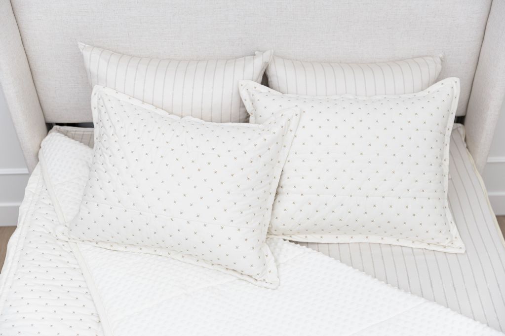 A bed made with cream embroidered zipper bedding with the comforter pulled back and pillows on top of the bed.