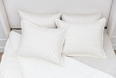 A bed made with cream embroidered zipper bedding with the comforter pulled back and pillows on top of the bed.