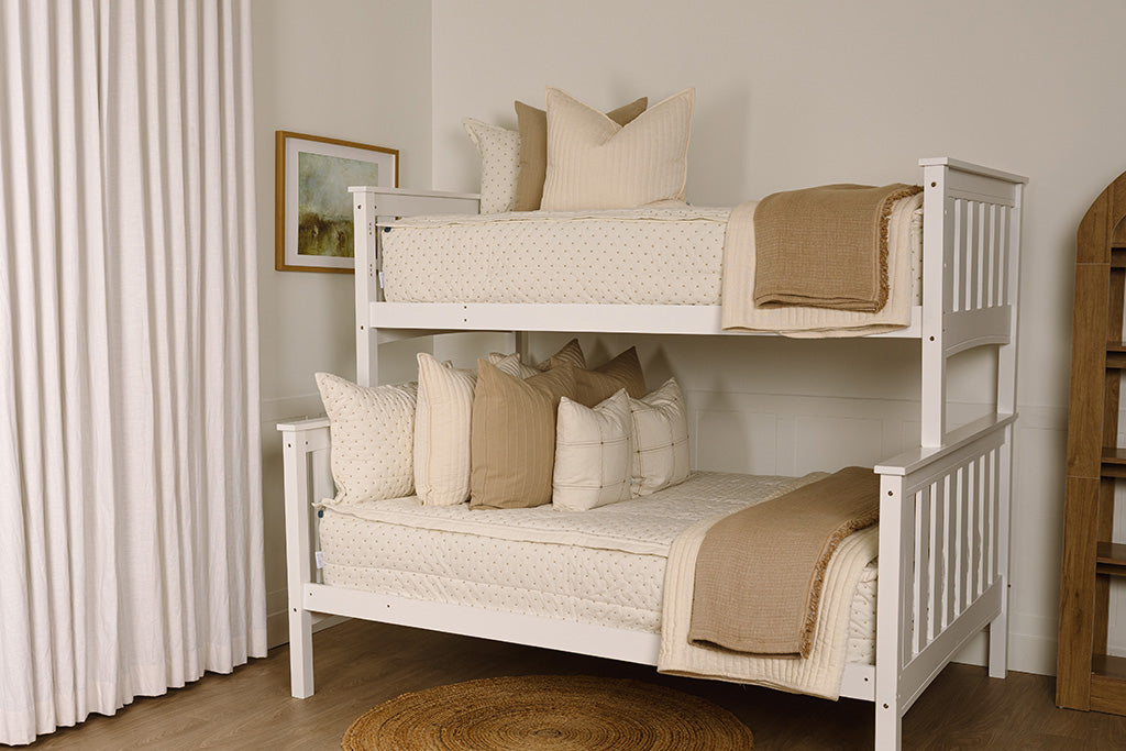 A bunk bed made with cream embroidered zipper bedding, decorated with neutral throw pillows and blankets.
