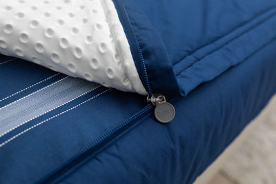 A close up view of a bed made with navy blue zipper bedding with the bed slightly unzipped to reveal the minky comforter and the striped navy blue pattern bottom cotton lining.