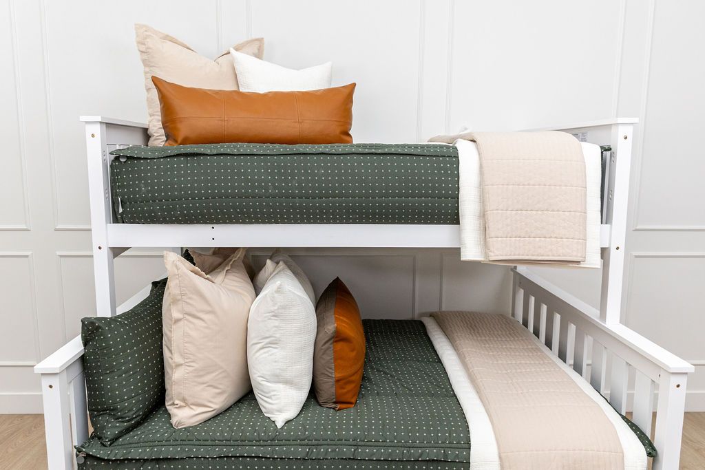 Bunk bed with dark green zipper bedding with small cross design paired with tan, cream and brown pillows and blankets
