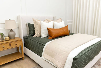 Queen bed with dark green zipper bedding with small cross design paired with tan, cream and brown pillows and blankets.