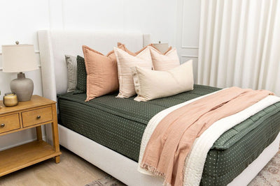 Queen bed with dark green zipper bedding with small cross design paired with terracotta, pink and tan pillows and blankets