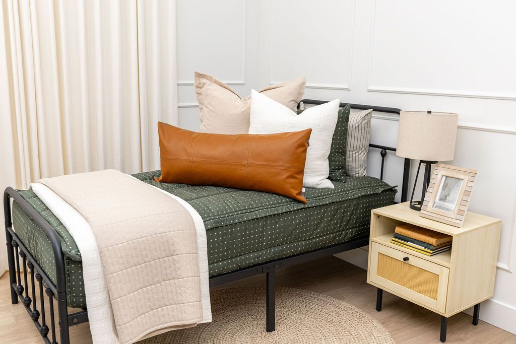 twin bed with Dark green zipper bedding with small cross design paired with tan, cream and brown pillows and blankets