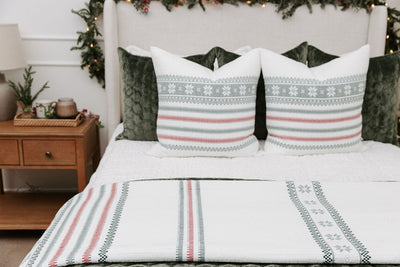 A bed made with seersucker white zipper bedding and an assortment of green velvet pillows and holiday striped pattern pillows and blankets.