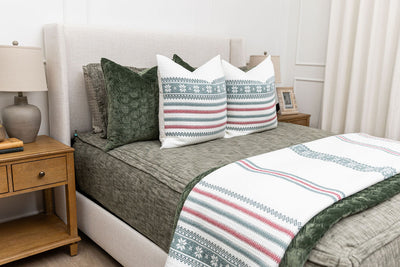A bed made with deep emerald green zipper bedding and an assortment of green velvet and holiday striped pillows and blankets.