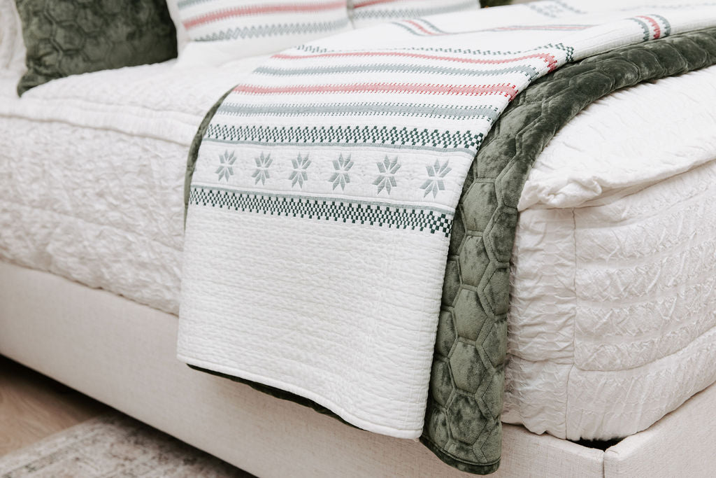 A side view of a bed made with seersucker white zipper bedding with a holiday striped white and velvet green blankets folded over the end of the bed.