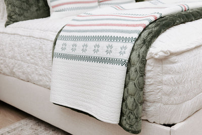 A side view of a bed made with seersucker white zipper bedding with a holiday striped white and velvet green blankets folded over the end of the bed.