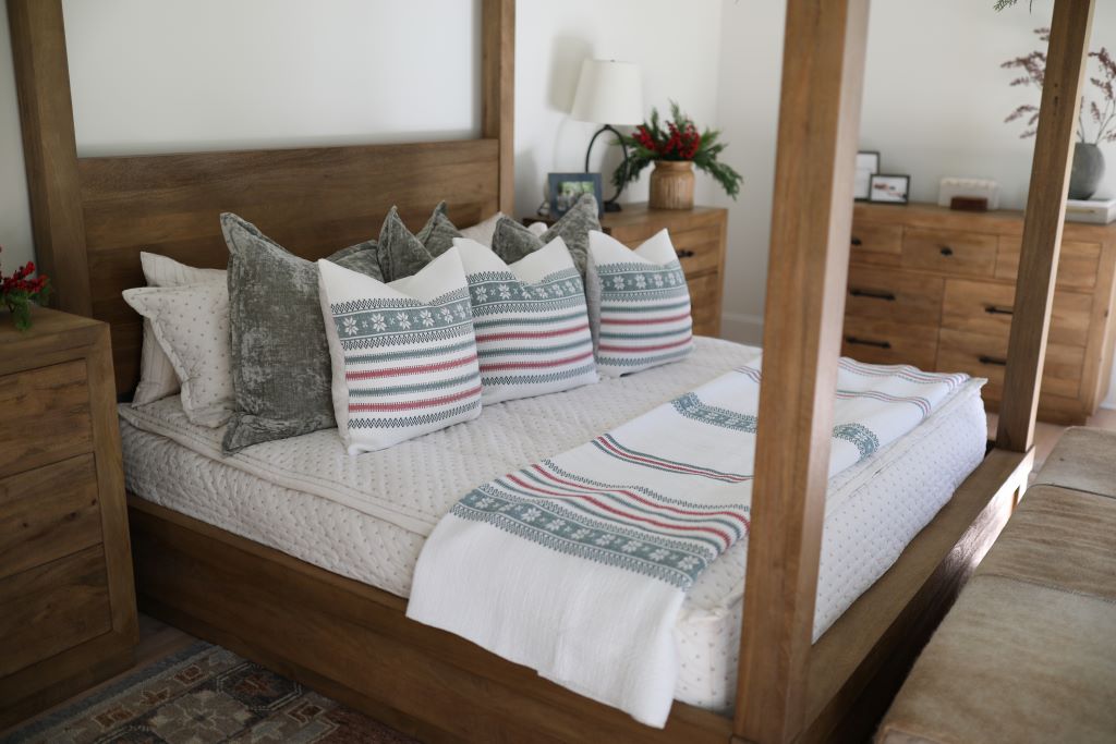 A bed made with cream embroidered zipper bedding and an assortment of green velvet pillows and holiday striped pattern pillows and blanket.