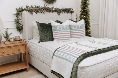 A side view of a bed made with seersucker white zipper bedding and an assortment of green velvet pillows and holiday striped pattern pillows and blankets. 