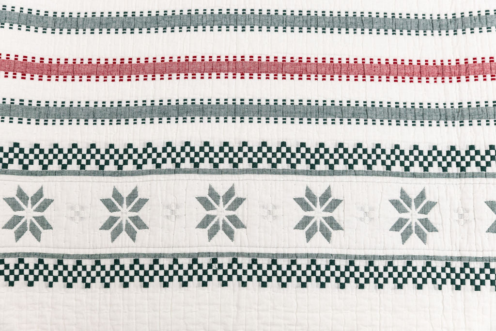 A close up view of a red, green, and snowflake striped pattern white holiday blanket.