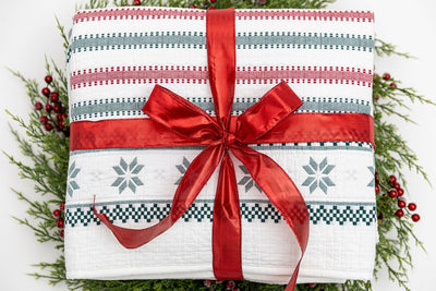 A red, green, and snowflake striped pattern white holiday blanket folded and wrapped in a red ribbon on top of a green wreath.