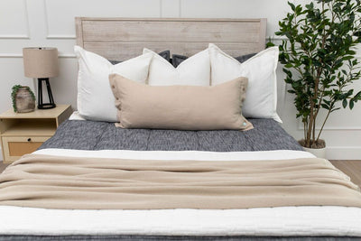 A close up view of a bed made with dark charcoal gray zipper bedding and neutral tan and white throw pillows and blankets.