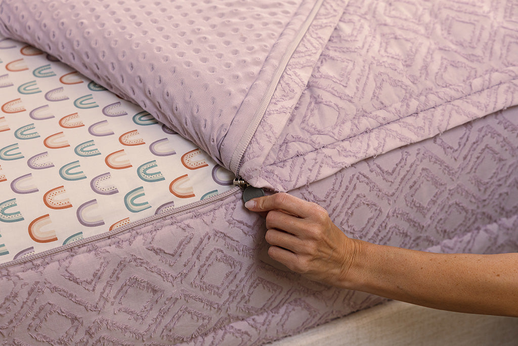 A close up view of a bed made with purple  zipper bedding.