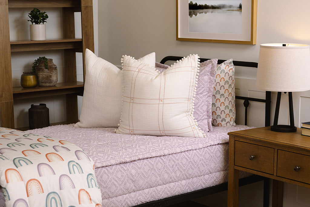 Twin bed with purple zipper bedding and rainbow and white accessories.