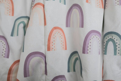 A close up of a peach, purple, light green pattern rainbow blanket.