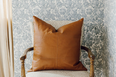 A neutral leather euro pillow with stitching arranged on a chair.