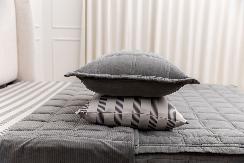 a gray sham stacked on top of a striped pillowcase, both sitting on top of a bed made with gray zipper bedding
