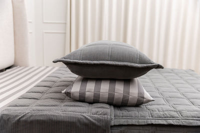 a gray sham stacked on top of a striped pillowcase, both sitting on top of a bed made with gray zipper bedding