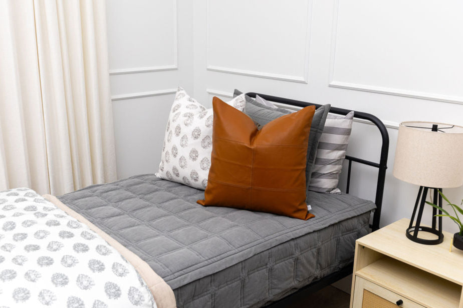 A twin bed made with gray zipper bedding  and an assortment of floral and leather pillows.