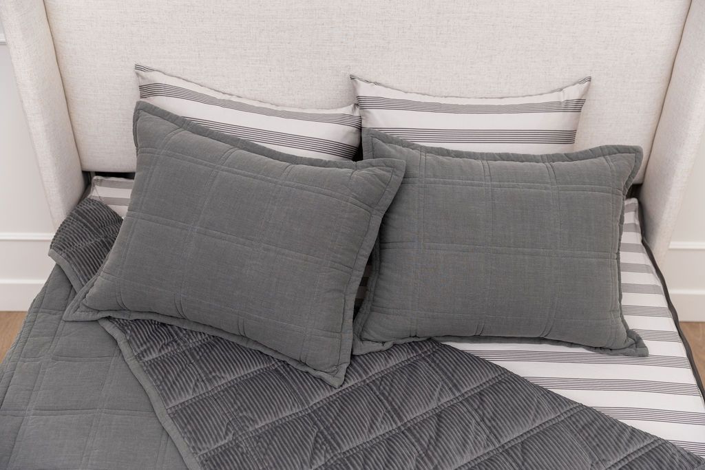 A bed made with gray zipper bedding with the top pulled back to reveal the inside lining, and four pillows arranged on top