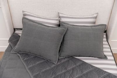 A bed made with gray zipper bedding with the top pulled back to reveal the inside lining, and four pillows arranged on top