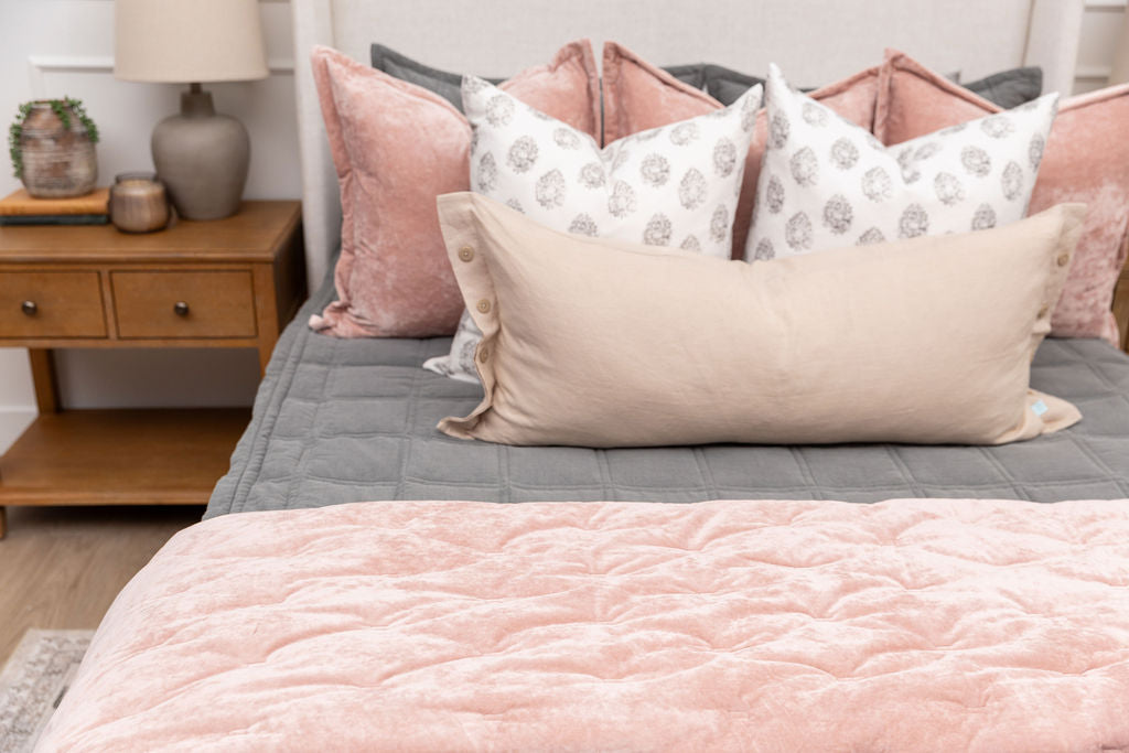 A queen bed made with gray zipper bedding and an assortment of pink and floral print bedding accessories