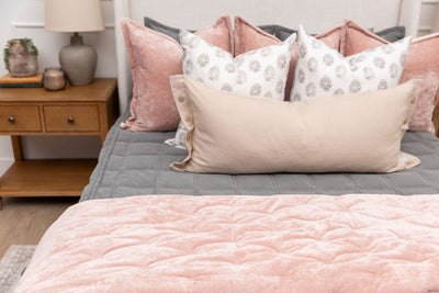 A queen bed made with gray zipper bedding and an assortment of pink and floral print bedding accessories