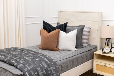 A twin bed made with gray zipper bedding and an assortment of neutral colored bedding accessories