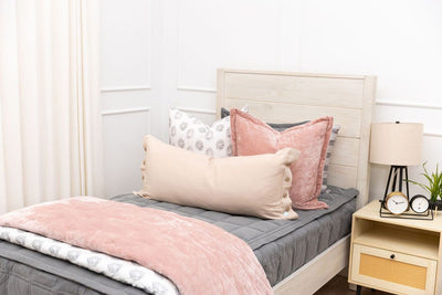 A twin bed made with gray zipper bedding and an assortment of floral and pink bedding accessories