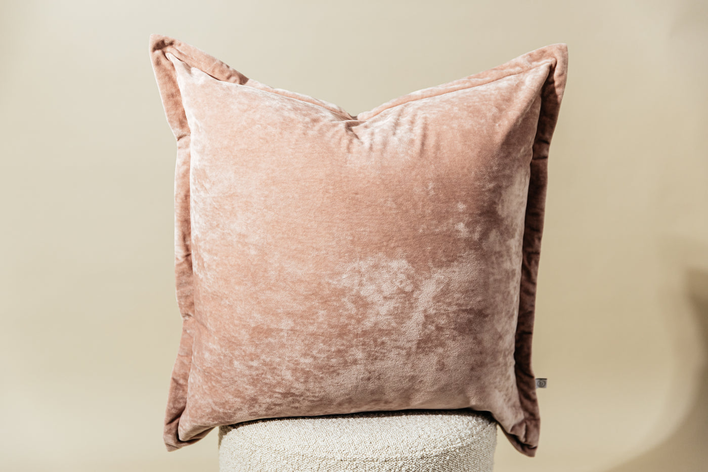 A pink velvet euro pillow arranged on a stool on a cream background.