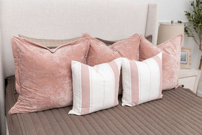A bed made with brown zipper bedding and an assortment of striped and pink velvet pillows.