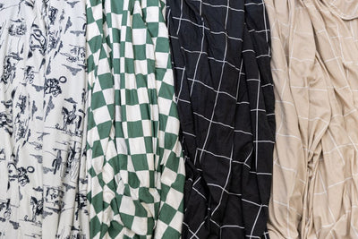 A close up look at four blankets laying side by side with different patterns including a western, a green and white checkered print, a charcoal grid pattern and a tan grid pattern.