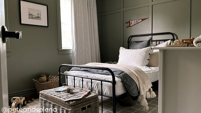 A twin bed made with white and pinstripes zipper bedding and dark charcoal gray and neutral pillows and blankets.