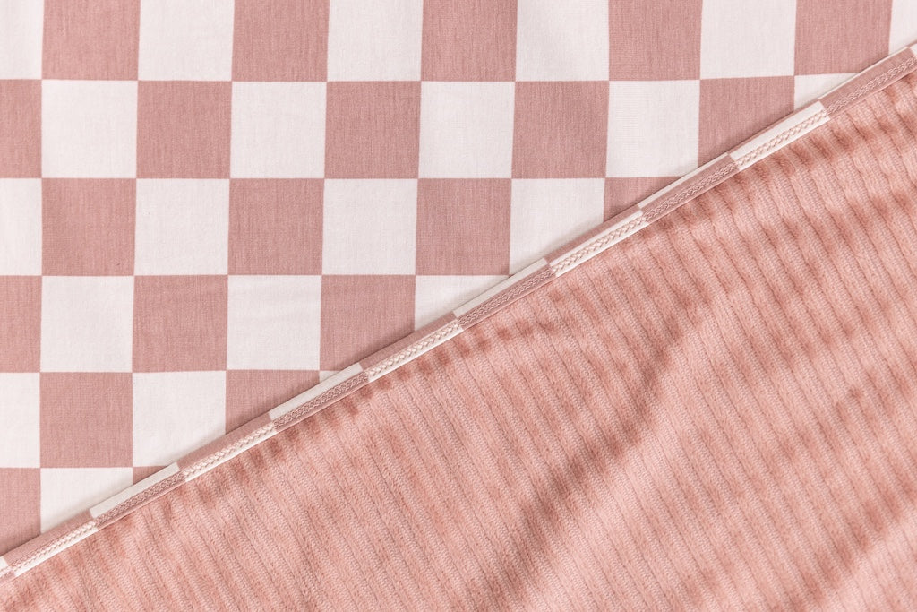 A close-up front and back view of a pink check printed travel blanket. 
