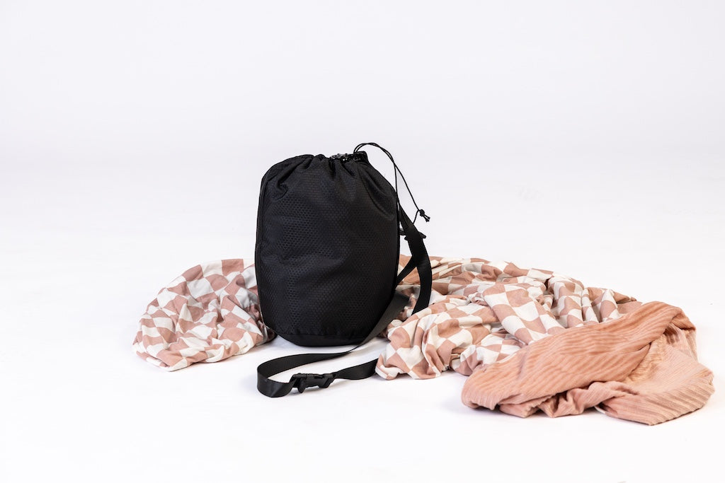 A pink check travel blanket laid on the ground around the travel blanket bag on a white background.