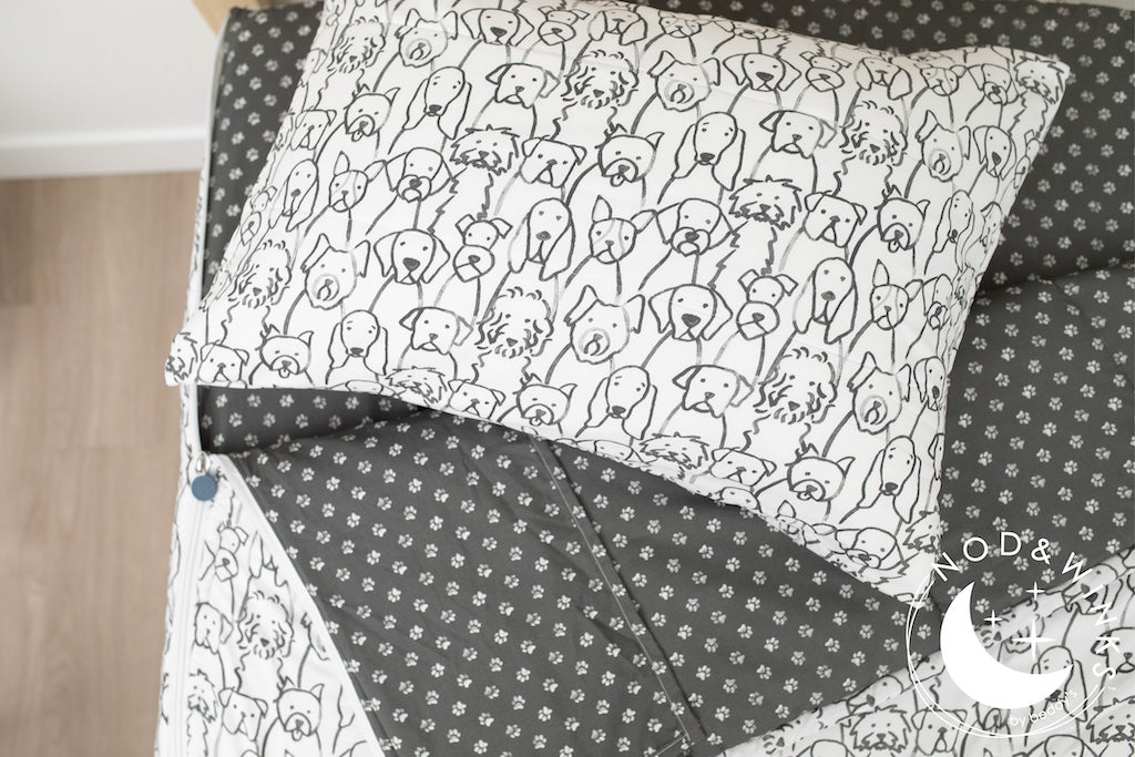 A twin bed made with charcoal and white pattern dogs kids zipper bedding, the top unzipped and slightly pulled back and a pillow on the bed.