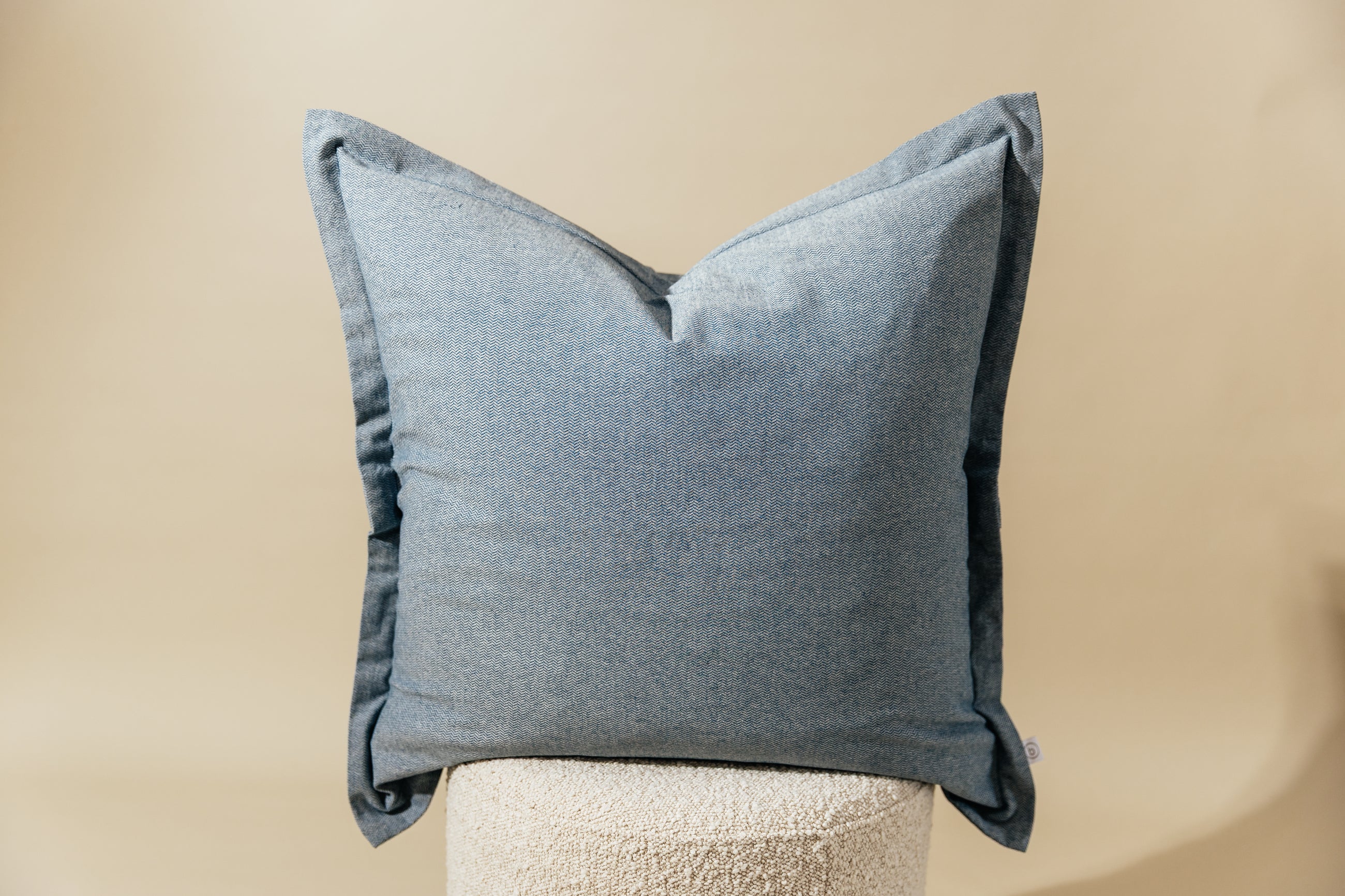 A blue two-toned herringbone euro pillow arranged on a cream stool with a cream background.