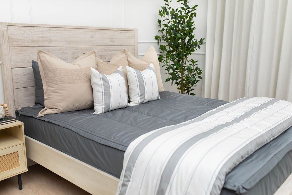 A bed made with gray zipper bedding and an assortment of neutral and striped throw pillows and blanket.