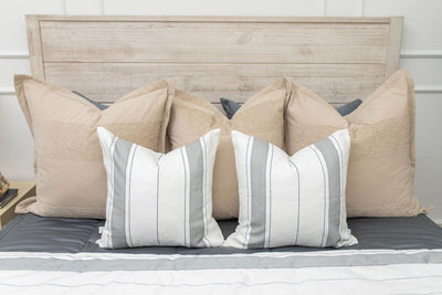 A close up view of a bed made with gray zipper bedding and an assortment of neutral and striped throw pillows and blanket.