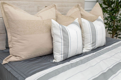 A side view of a bed made with gray zipper bedding and an assortment of neutral and striped throw pillows and blanket.