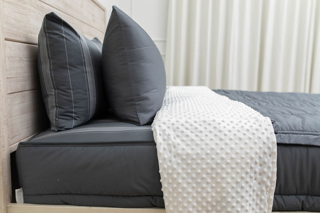A side view of a bed made with gray zipper bedding with the top unzipped halfway down the bed and the comforter folded down.