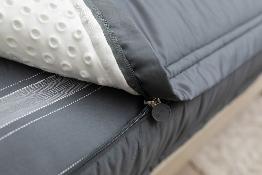 A close up view of a bed made with gray zipper bedding with the bed slightly unzipped to reveal the minky comforter and the striped gray pattern bottom cotton lining.