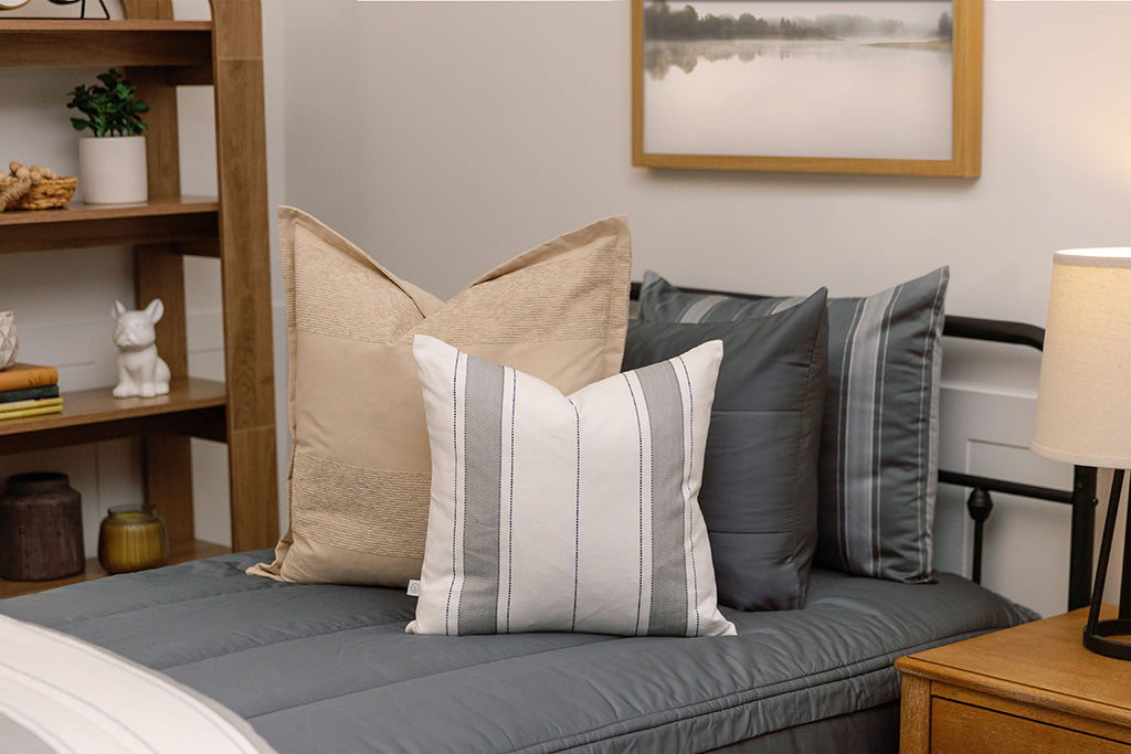 A twin bed made with gray zipper bedding and gray striped pillow and blanket.