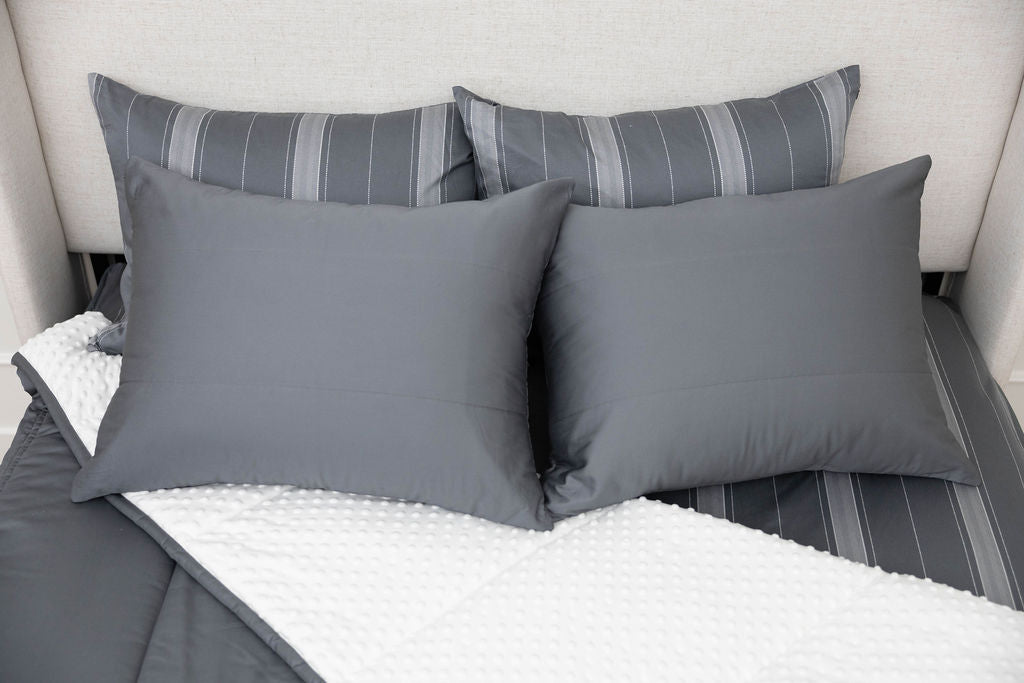 A bed made with gray zipper bedding with the comforter pulled back and pillows on top of the bed.