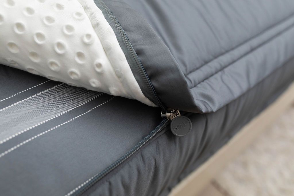 A close up view of a bed made with gray zipper bedding with the bed slightly unzipped to reveal the minky comforter and the striped gray pattern bottom cotton lining.