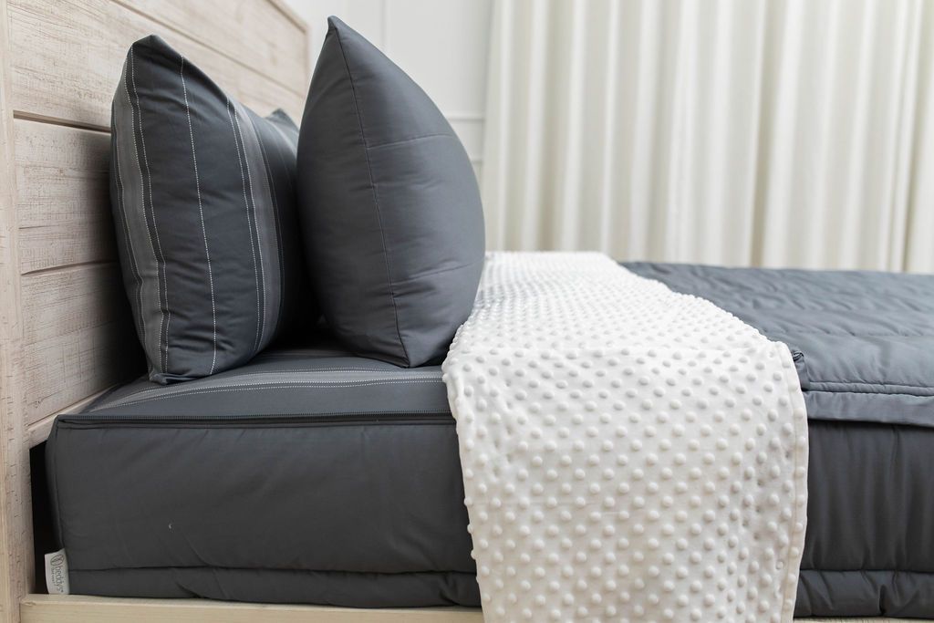 A side view of gray zipper bedding on a bed with the top unzipped halfway down and the comforter folded down.